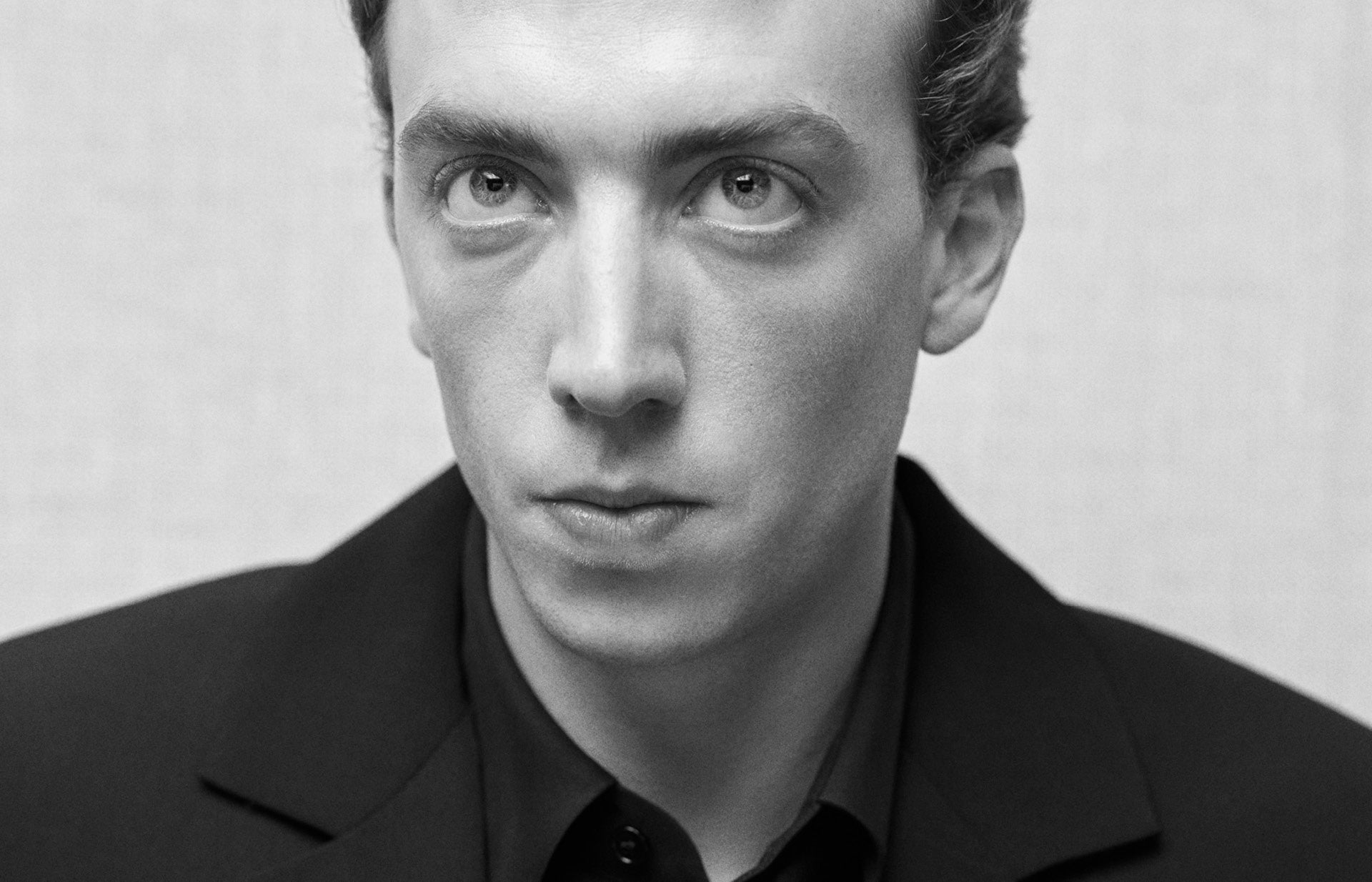 Black and white portrait of a person wearing a dark suit against a plain background
